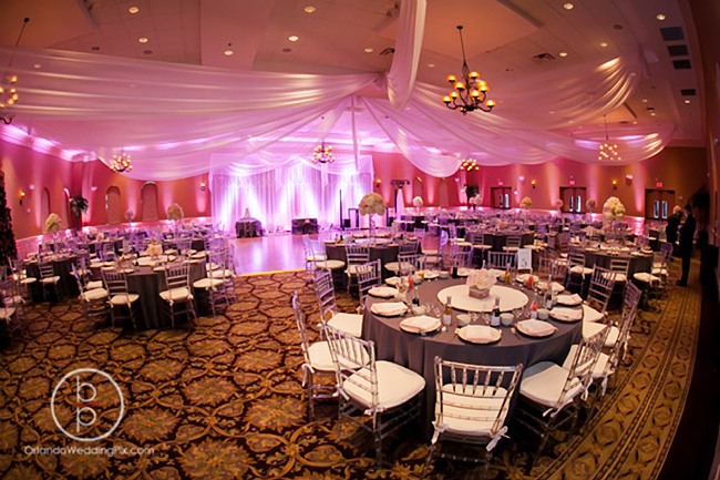 Custom event draping, and backdrop in white chiffon with decorative strings of crystal beads, chandeliers, and LED up-lights for a modern wedding reception at Holy Trinity Reception Center in Maitland, FL. Chiffon drapes and accessories by W Drapings. Photo by Brian Pepper of OrlandoWeddingPix.